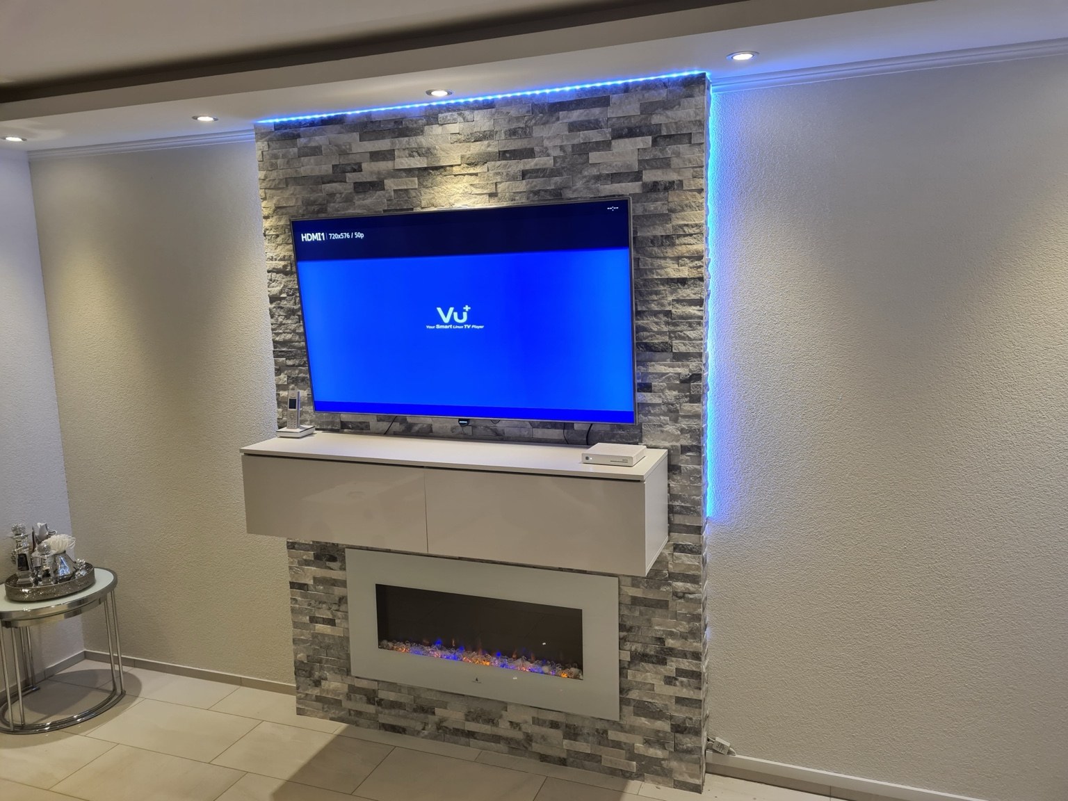 Wandgestaltung in Steinoptik mit integriertem Kamin und seitlichen LED-Lichtakzenten.